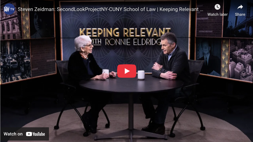 two people sit at a table for a TV interview